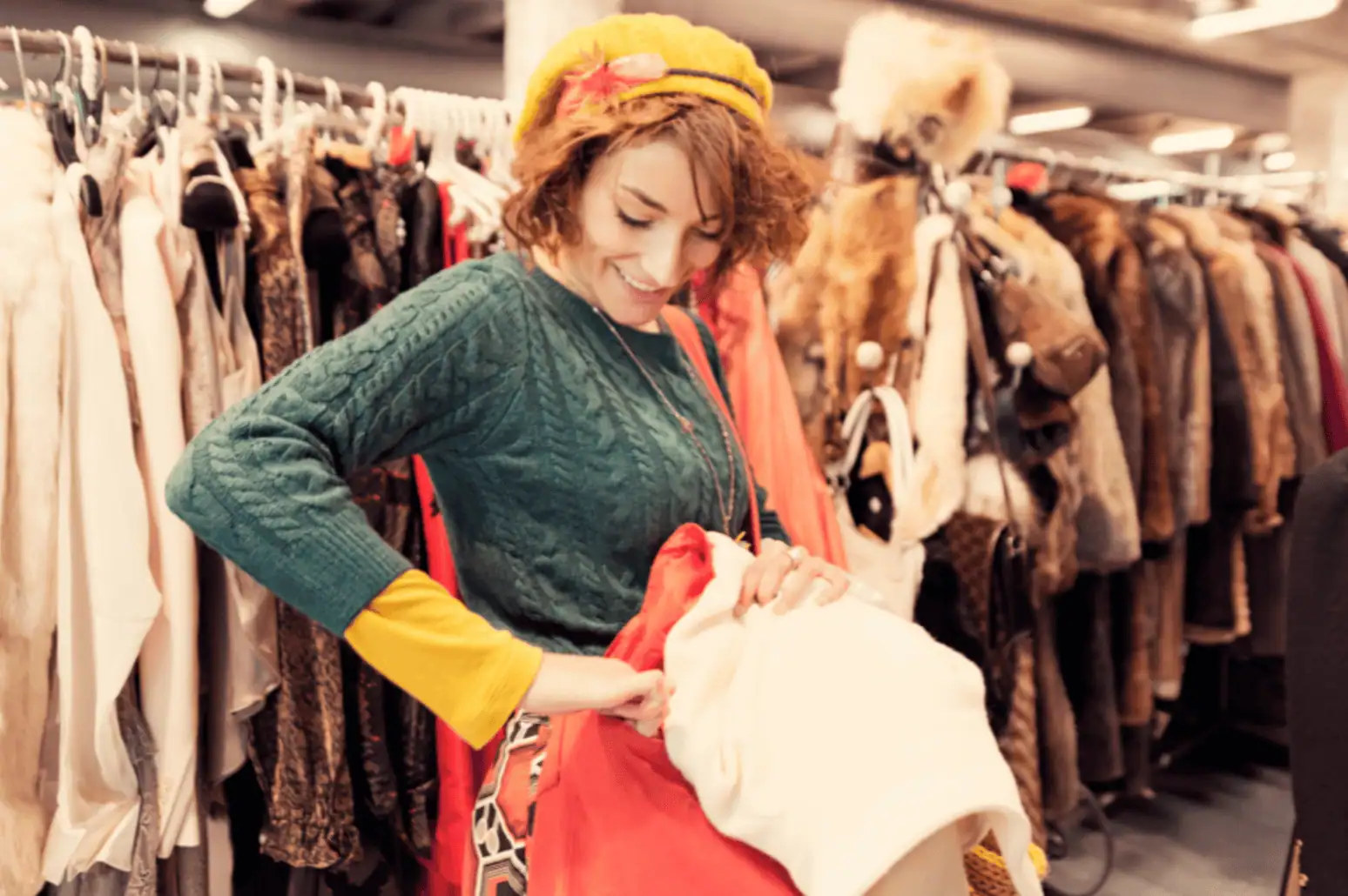 happy woman in sweater with vintage hat, holding up a thrift store find