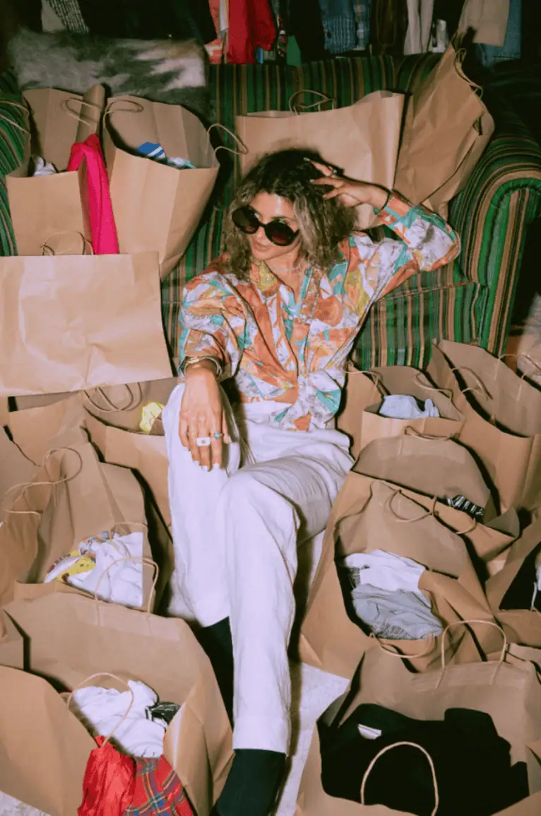 vintage gal wearing sunglasses sitting in a pile of bags of clothes