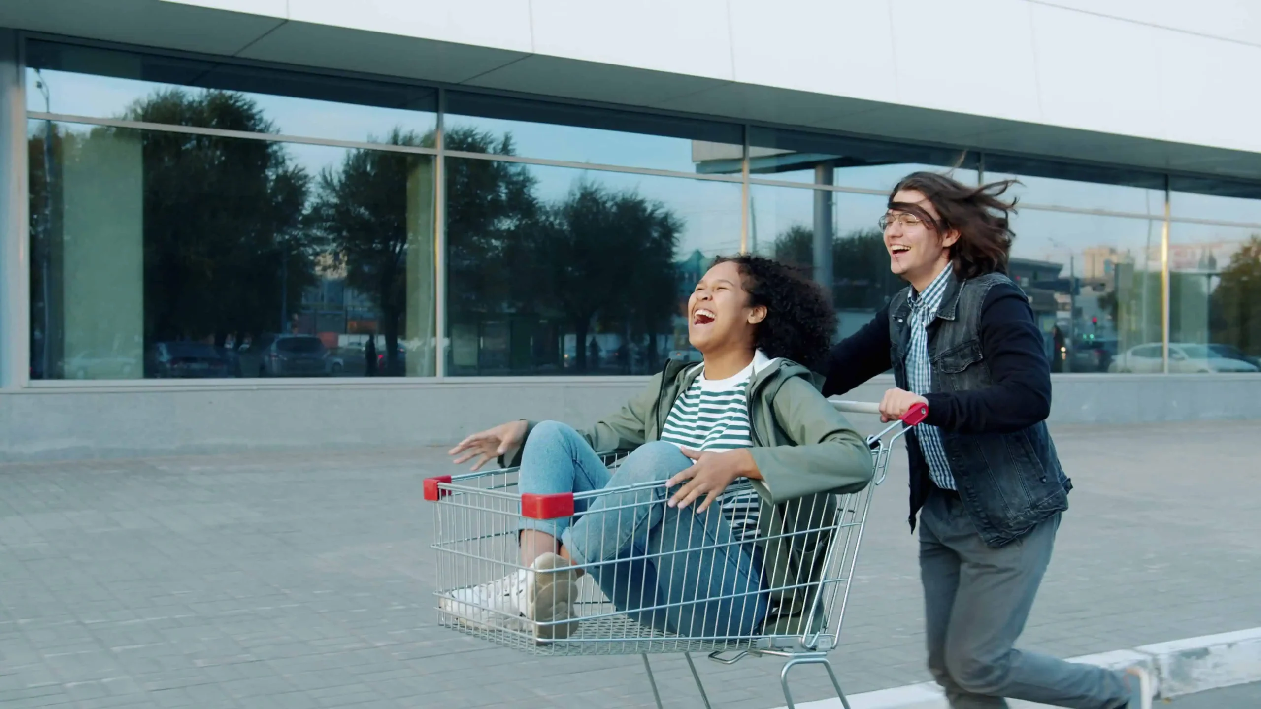 one person pushing another laughing person who is riding in a shopping cart