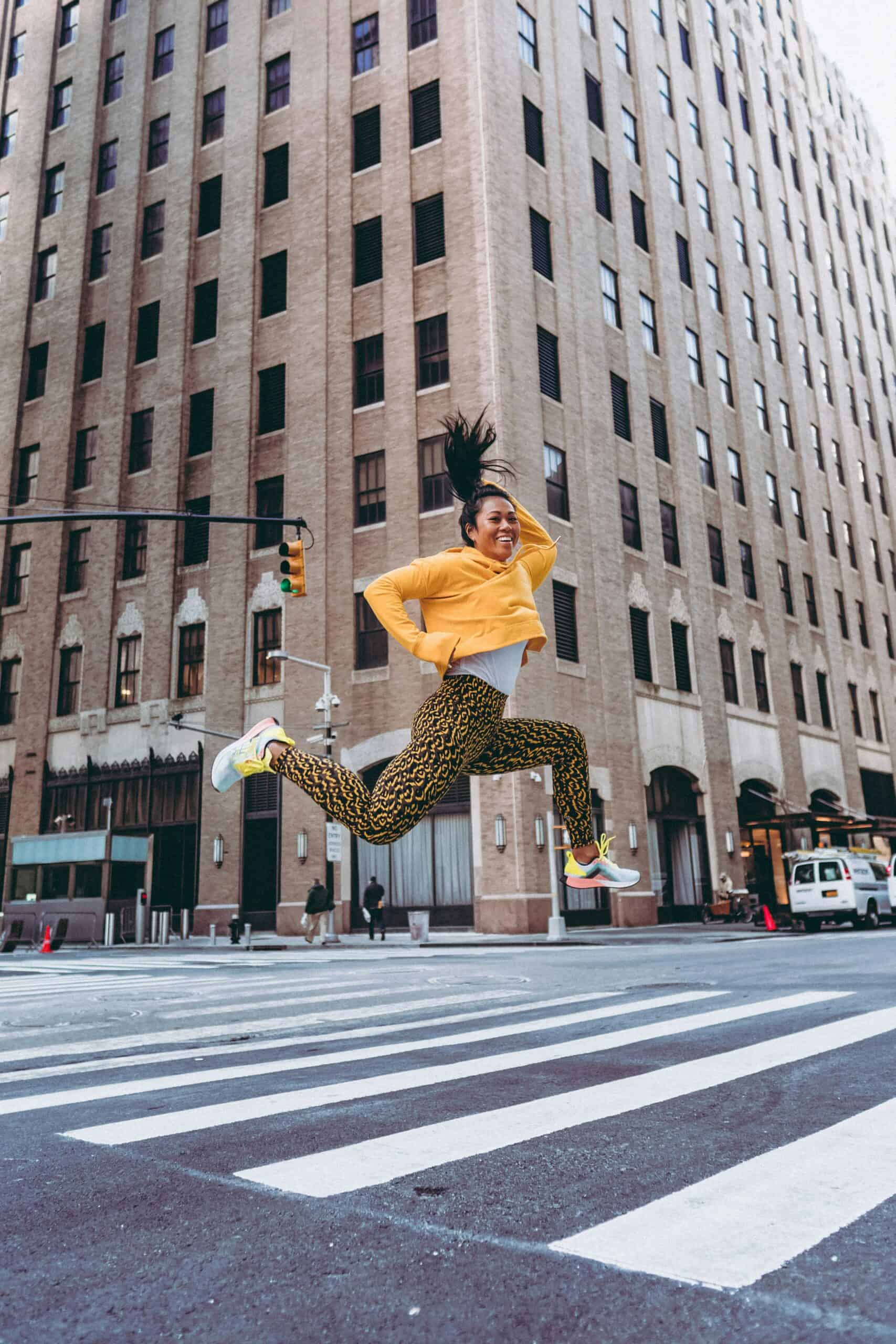 Jumping woman in colorful workout gear on city street, showcasing energetic fitness and urban style.