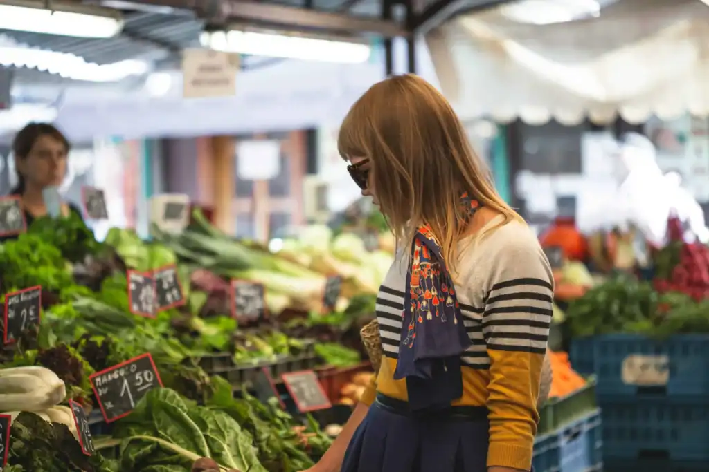 A stylish shopper wearing sunglasses and a neck scarf browsing produce.